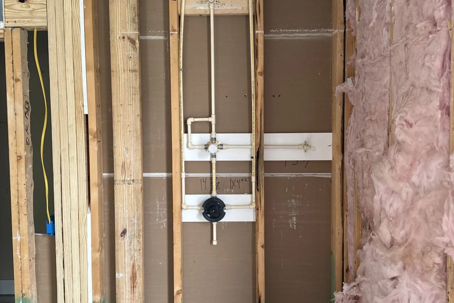 Open bathroom wall with new CPVC supply lines run to a shower valve during a repipe