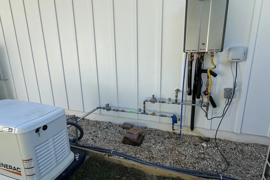 Outdoor Rinnai tankless water heater mounted on a white board and batten wall beside a standby generator